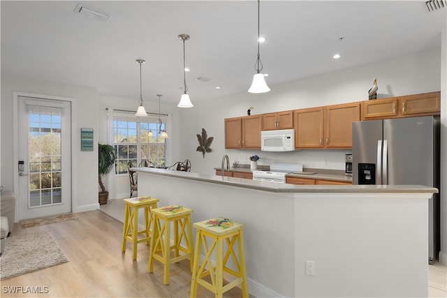 kitchen with an island with sink, decorative light fixtures, white appliances, a breakfast bar area, and light wood-type flooring