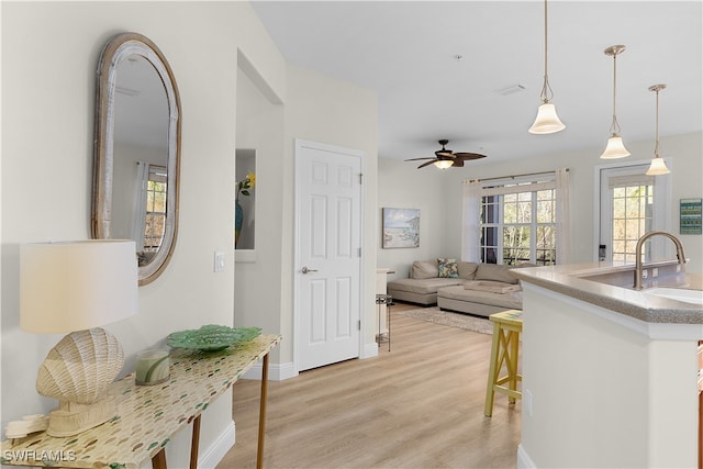 kitchen featuring pendant lighting, a breakfast bar, sink, ceiling fan, and light hardwood / wood-style floors