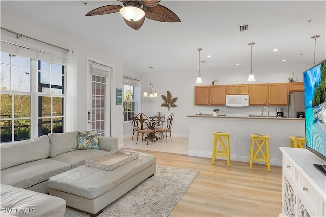 living room featuring ceiling fan with notable chandelier, a healthy amount of sunlight, light wood-type flooring, and sink