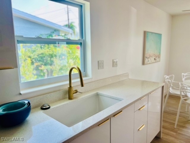 kitchen featuring white cabinets, light stone counters, wood-type flooring, and sink