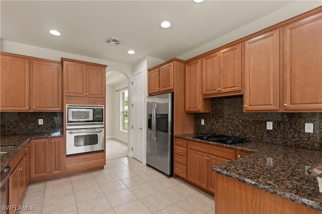 kitchen featuring stainless steel appliances, light tile patterned floors, backsplash, and dark stone counters