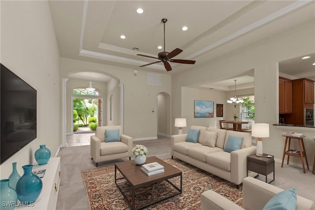 living room with ceiling fan with notable chandelier, plenty of natural light, and a raised ceiling