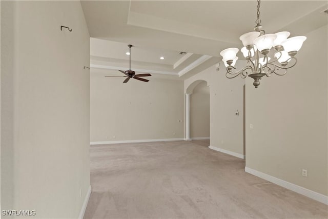 empty room with baseboards, light colored carpet, ceiling fan with notable chandelier, arched walkways, and a raised ceiling