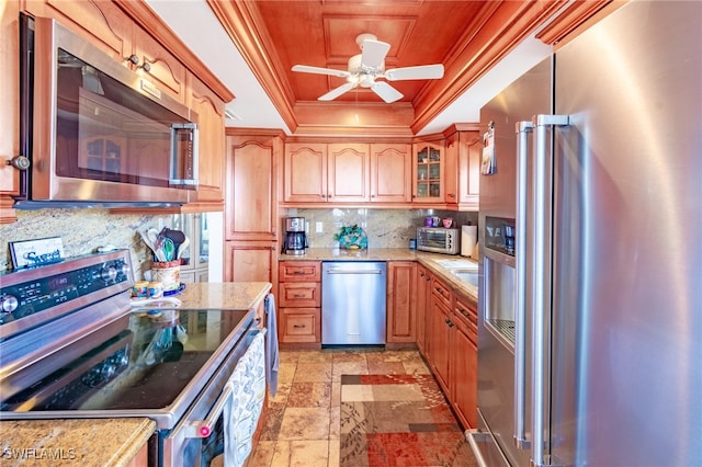 kitchen featuring decorative backsplash, appliances with stainless steel finishes, light stone countertops, ornamental molding, and a tray ceiling