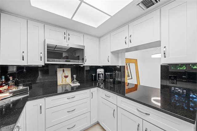 kitchen with backsplash, dark stone countertops, and white cabinetry