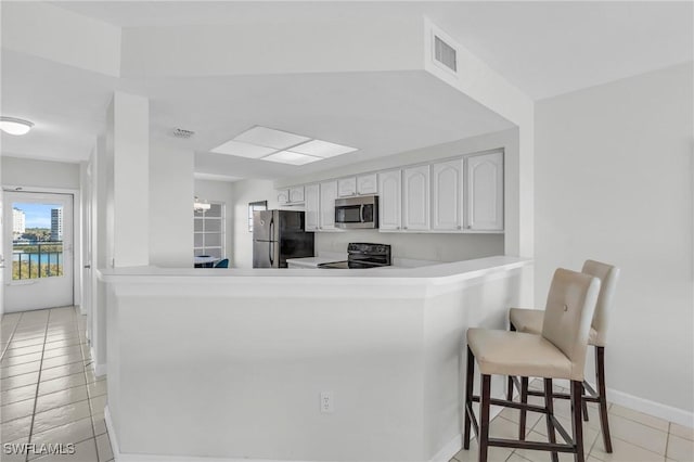 kitchen with white cabinets, appliances with stainless steel finishes, kitchen peninsula, a breakfast bar, and light tile patterned floors