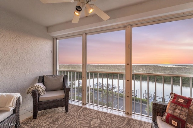 sunroom featuring ceiling fan and a water view