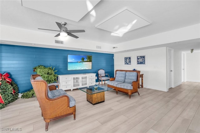 living room featuring ceiling fan, light hardwood / wood-style flooring, and wood walls