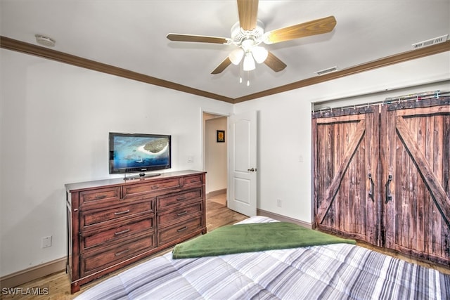 bedroom with ceiling fan, a barn door, ornamental molding, and light hardwood / wood-style flooring