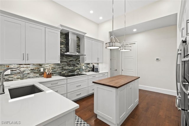 kitchen with wood counters, black electric stovetop, sink, wall chimney exhaust hood, and a kitchen island