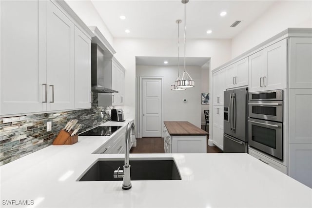 kitchen featuring butcher block counters, wall chimney exhaust hood, hanging light fixtures, stainless steel appliances, and tasteful backsplash