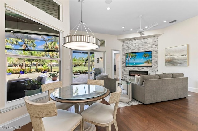 dining room featuring a stone fireplace, ceiling fan, and dark hardwood / wood-style floors