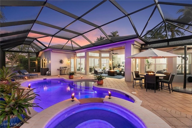 pool at dusk featuring glass enclosure, an in ground hot tub, a patio area, and ceiling fan