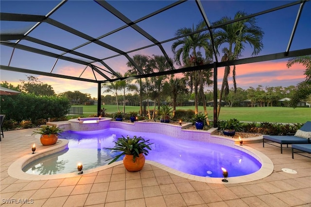 pool at dusk with an in ground hot tub, a patio area, a lanai, and a lawn