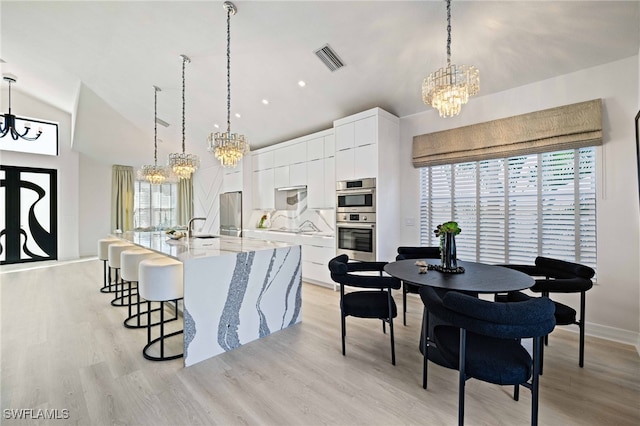 kitchen with a large island with sink, white cabinets, hanging light fixtures, and appliances with stainless steel finishes