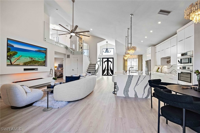 living room featuring high vaulted ceiling, ceiling fan with notable chandelier, and light wood-type flooring