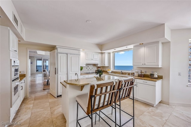 kitchen featuring white cabinets, a kitchen breakfast bar, a water view, and light stone counters