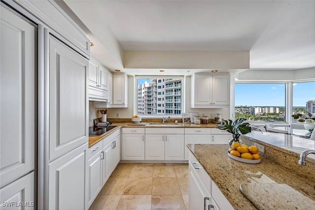 kitchen featuring black electric cooktop, light stone countertops, white cabinets, and a healthy amount of sunlight