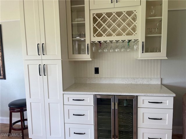 bar featuring white cabinets, light stone counters, and beverage cooler