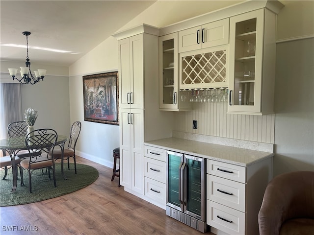 bar with light stone countertops, decorative light fixtures, hardwood / wood-style flooring, wine cooler, and lofted ceiling