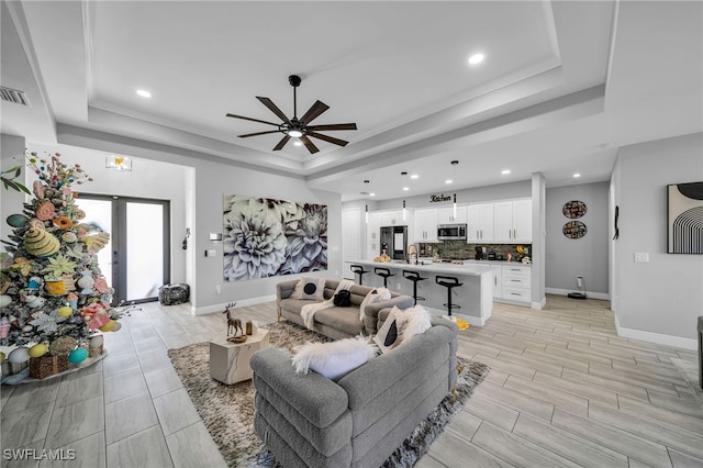 living room featuring french doors, a raised ceiling, ceiling fan, and sink