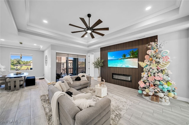 living room with a tray ceiling, ceiling fan, and light wood-type flooring