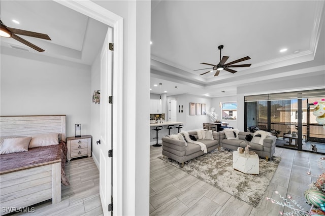 living room with a tray ceiling, ceiling fan, crown molding, and light wood-type flooring