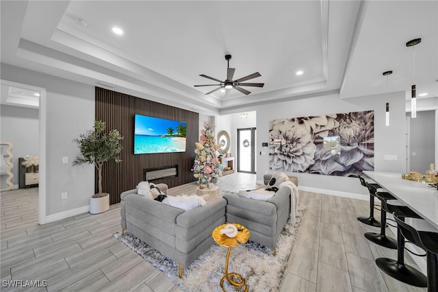 living room with ceiling fan, a raised ceiling, and light wood-type flooring