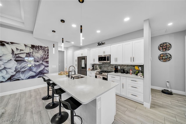 kitchen with stainless steel appliances, sink, decorative light fixtures, white cabinets, and an island with sink