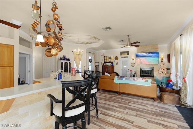 dining space with ceiling fan with notable chandelier, a large fireplace, wood-type flooring, and ornamental molding