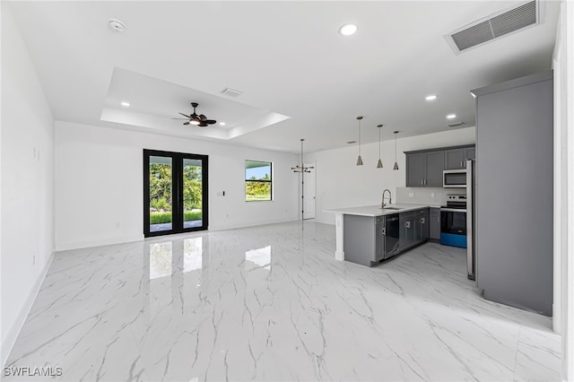 kitchen featuring sink, stainless steel appliances, a raised ceiling, pendant lighting, and ceiling fan with notable chandelier