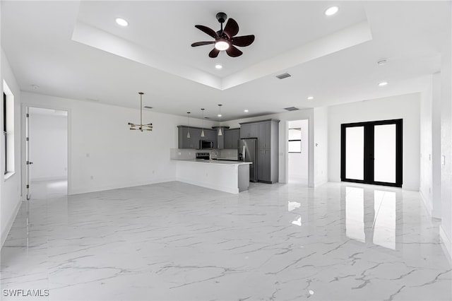 unfurnished living room with a tray ceiling, ceiling fan, and french doors