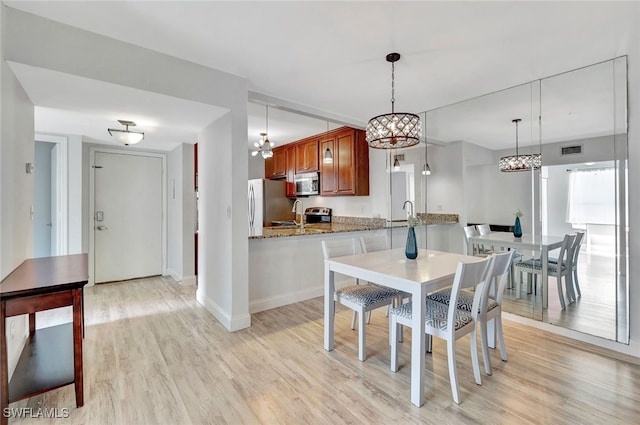 dining space with sink, light hardwood / wood-style floors, and an inviting chandelier