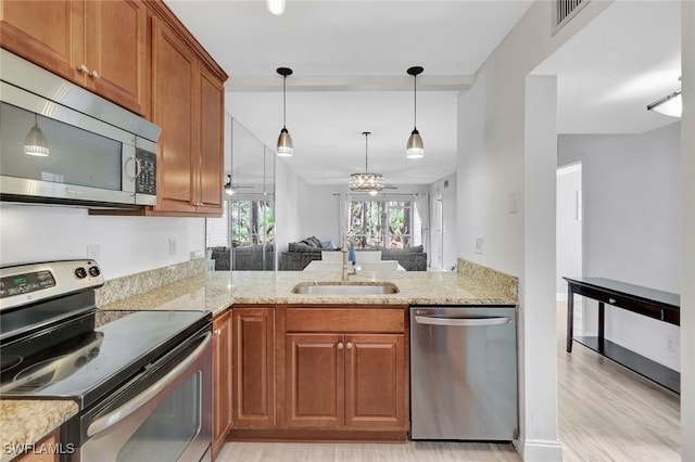 kitchen with kitchen peninsula, appliances with stainless steel finishes, light wood-type flooring, sink, and hanging light fixtures