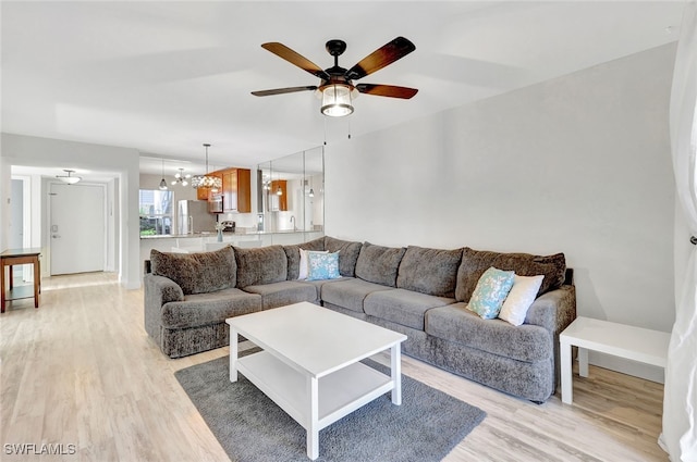 living room with ceiling fan with notable chandelier and light hardwood / wood-style floors