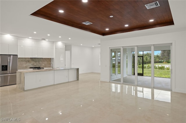 kitchen with wooden ceiling, stainless steel appliances, a tray ceiling, a center island with sink, and white cabinets