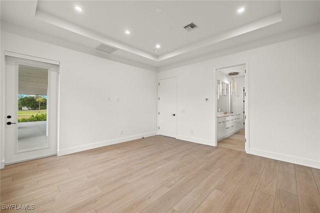 unfurnished bedroom featuring access to exterior, connected bathroom, a tray ceiling, and light hardwood / wood-style flooring