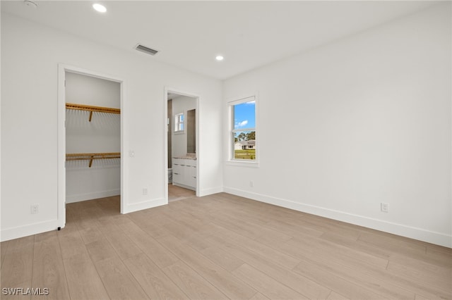 unfurnished bedroom with a walk in closet, ensuite bathroom, and light hardwood / wood-style floors