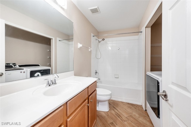 full bathroom with washing machine and dryer, toilet, hardwood / wood-style flooring, vanity, and tiled shower / bath