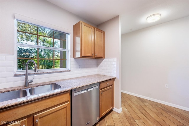 kitchen with sink, light stone counters, stainless steel dishwasher, decorative backsplash, and light wood-type flooring