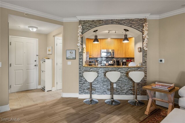 kitchen featuring tasteful backsplash, crown molding, decorative light fixtures, appliances with stainless steel finishes, and light wood-type flooring