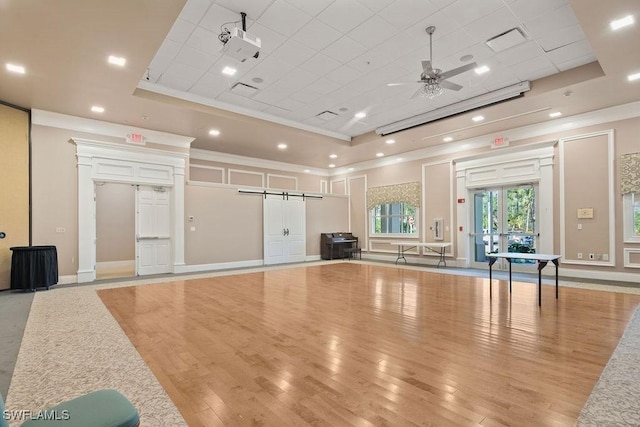 exercise area with a raised ceiling, ceiling fan, and light wood-type flooring