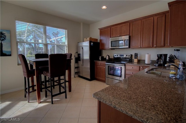 kitchen with dark stone counters, a kitchen breakfast bar, sink, light tile patterned floors, and stainless steel appliances