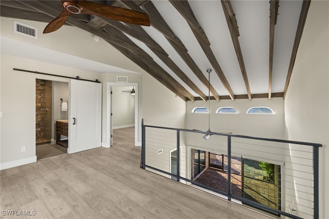 interior space with a barn door, light hardwood / wood-style flooring, beamed ceiling, and high vaulted ceiling