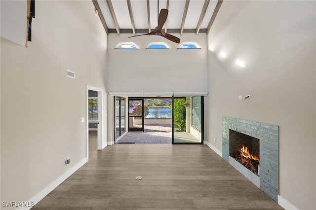 foyer with wood-type flooring, high vaulted ceiling, a wealth of natural light, and a stone fireplace