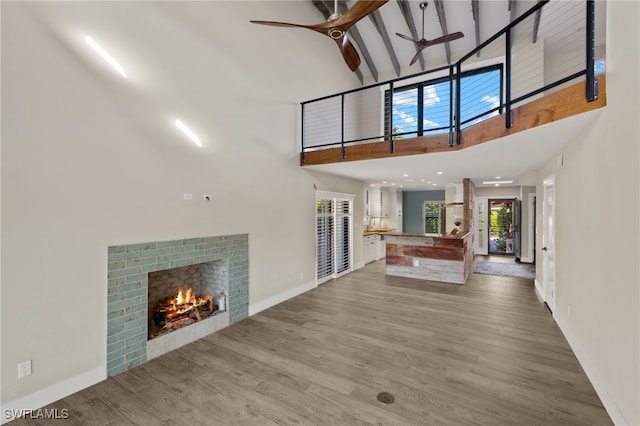 unfurnished living room with ceiling fan, hardwood / wood-style flooring, high vaulted ceiling, beamed ceiling, and a fireplace