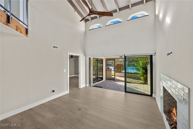 unfurnished living room featuring beamed ceiling, a brick fireplace, light hardwood / wood-style flooring, and high vaulted ceiling