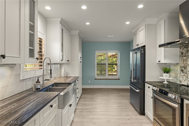 kitchen with decorative backsplash, light wood-type flooring, wall chimney exhaust hood, stainless steel appliances, and white cabinetry