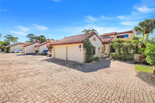 mediterranean / spanish-style home featuring a tile roof, decorative driveway, a garage, and stucco siding