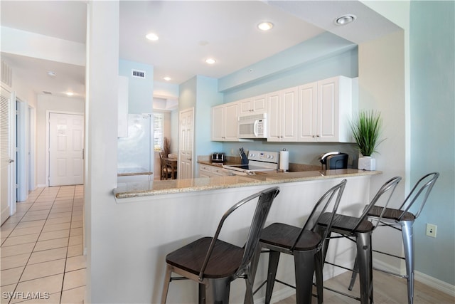 kitchen with white cabinets, light stone counters, white appliances, and kitchen peninsula